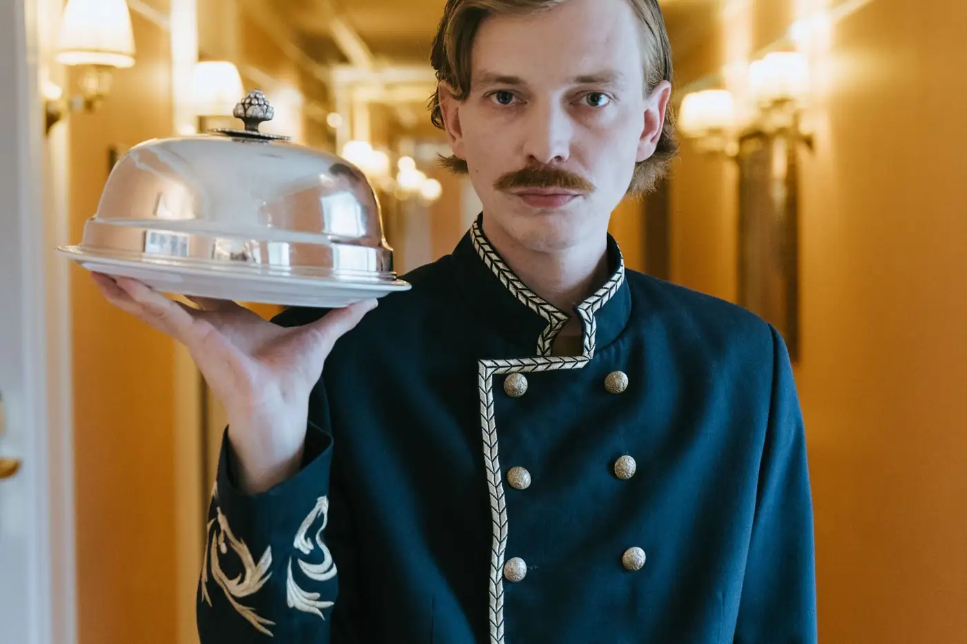 Un chasseur d'hôtel porte une cloche d'argent.