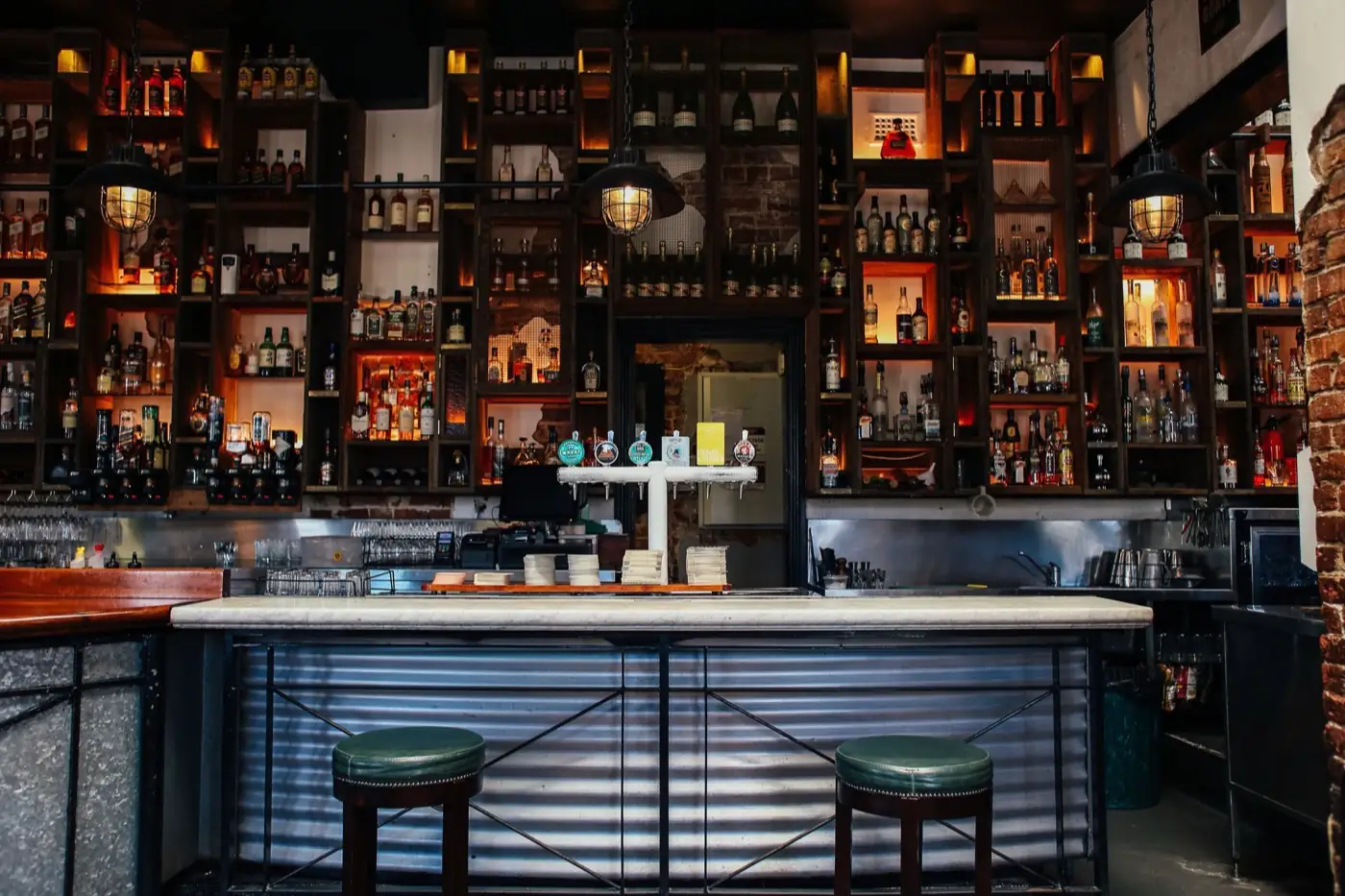Le comptoir d'un bar et ses étagères de bouteilles.